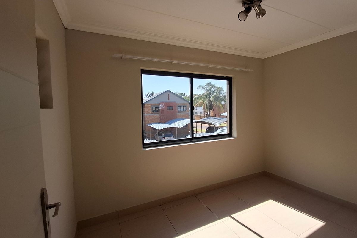 A bright, empty bedroom featuring neutral tiled flooring, a sliding window, and a ceiling-mounted light fixture, offering a clean canvas for personalization.