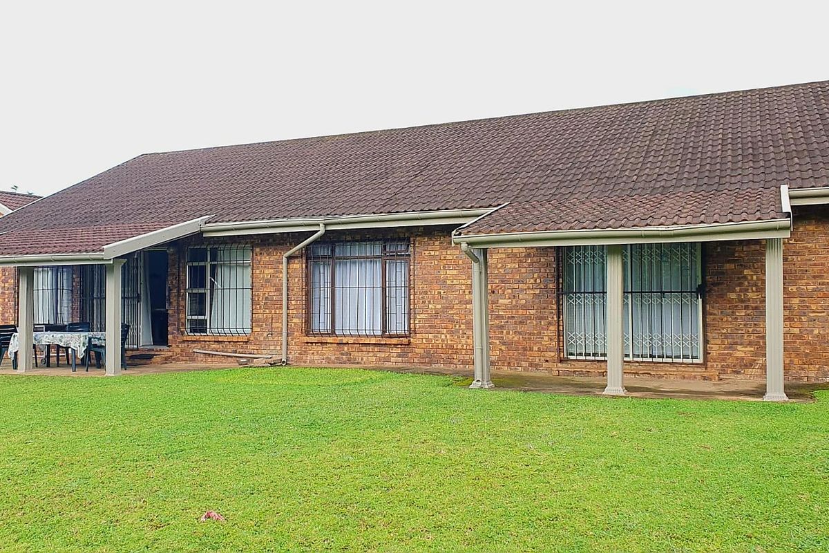 Rear view of a single-story brick house featuring a covered patio area, tiled roof, and security bars on windows and doors.