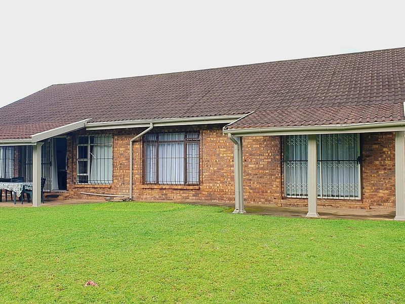 Rear view of a single-story brick house featuring a covered patio area, tiled roof, and security bars on windows and doors.