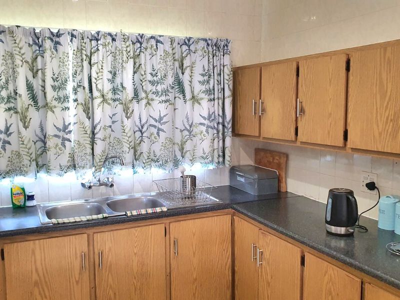 A functional kitchen featuring wooden cabinetry, laminate countertops, and a double bowl sink with a tiled splashback, offering a classic, dated aesthetic.