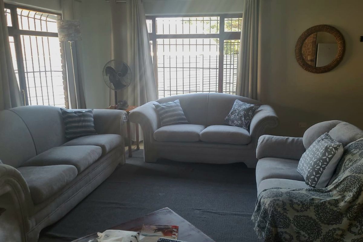 A living room featuring large windows with security bars and neutral wall finishes, offering a functional space for relaxation.