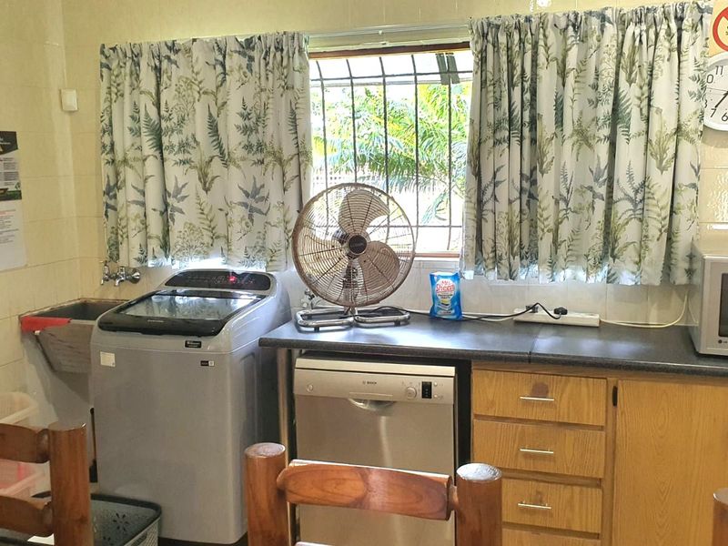 Functional laundry area featuring tiled walls, built-in cabinetry with laminate countertops, an integrated dishwasher, and a utility sink.