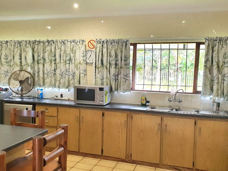 A functional kitchen featuring wood-look cabinetry, laminate countertops, a double basin sink, and tiled flooring, with security bars installed on the window.
