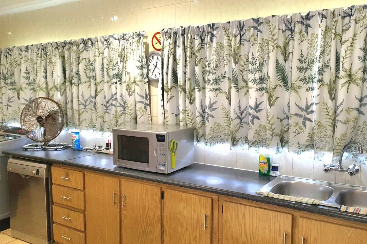 A functional kitchen area featuring timber cabinetry, laminate countertops, and a double bowl stainless steel sink with wall-mounted tapware.