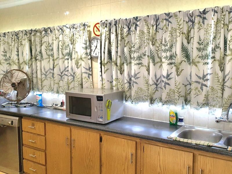 A functional kitchen area featuring timber cabinetry, laminate countertops, and a double bowl stainless steel sink with wall-mounted tapware.