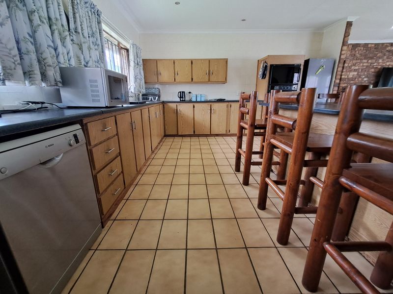 A functional kitchen featuring wooden cabinetry, tiled flooring, and a breakfast bar, offering a classic layout with potential for modern updates.