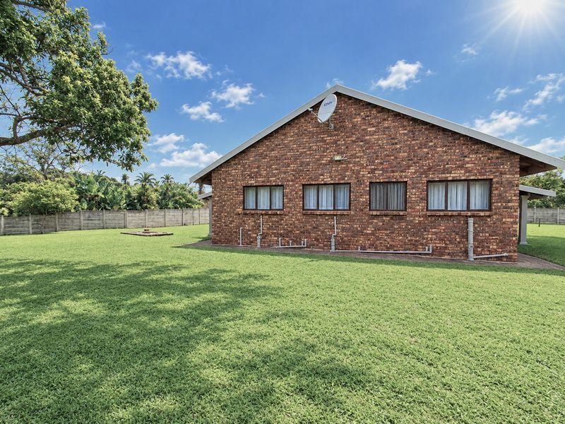 Rear view of the face brick house featuring a large lawn, paved perimeter, and boundary walling.