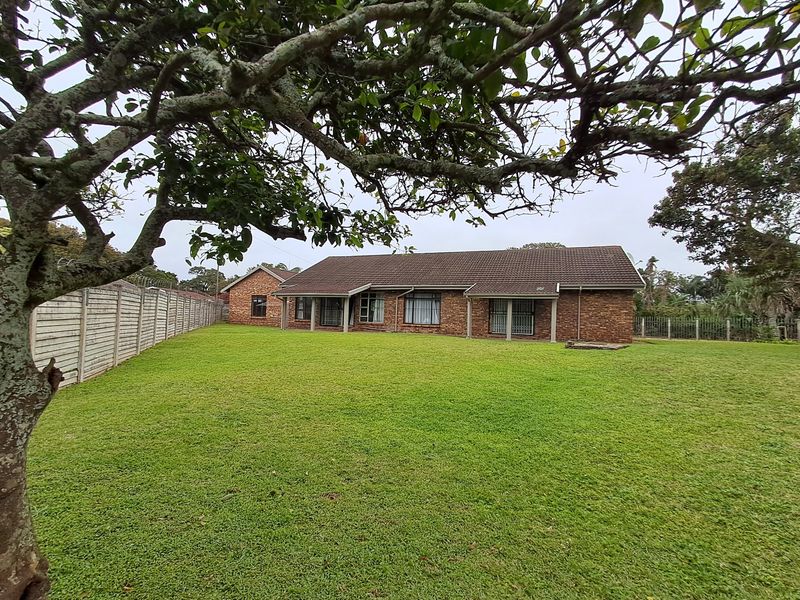 A spacious rear garden featuring a large lawn, mature trees, and a brick-faced house with a tiled roof and security-fitted windows.