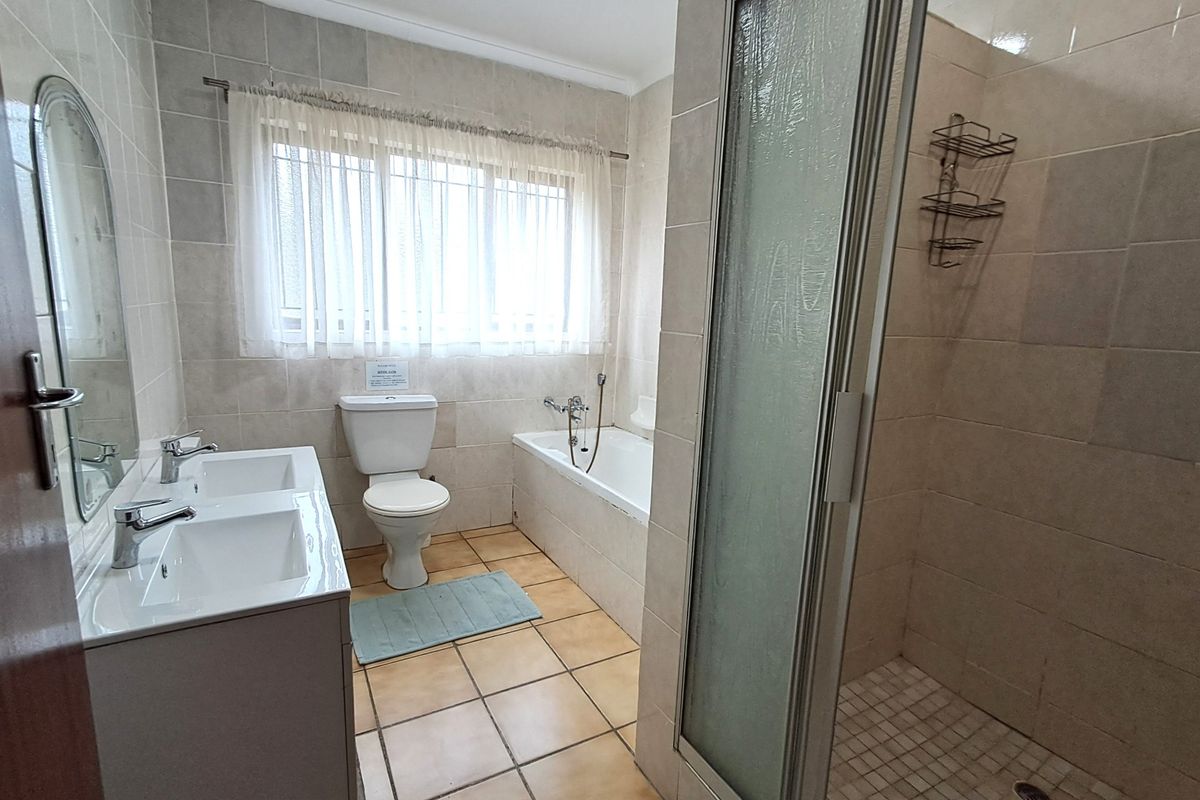 A functional bathroom featuring a double vanity, a built-in bathtub, and a separate shower enclosure with neutral wall and floor tiling.