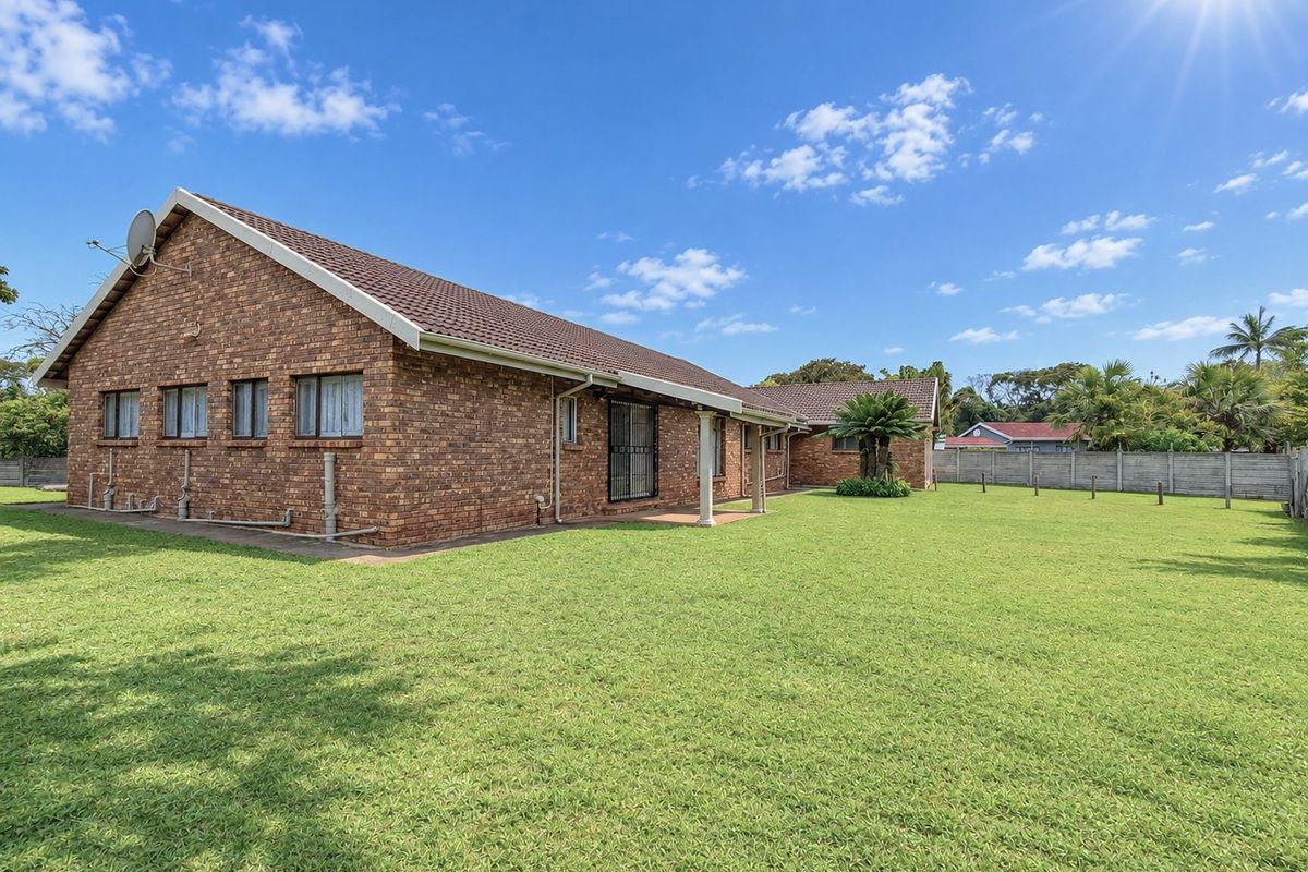 Spacious rear exterior view of a face brick house featuring a large lawn, covered patio area, and secure boundary walling.