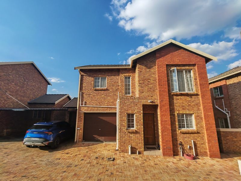 Front elevation of a double-storey face-brick townhouse featuring a single garage, paved driveway, and secure window fittings.