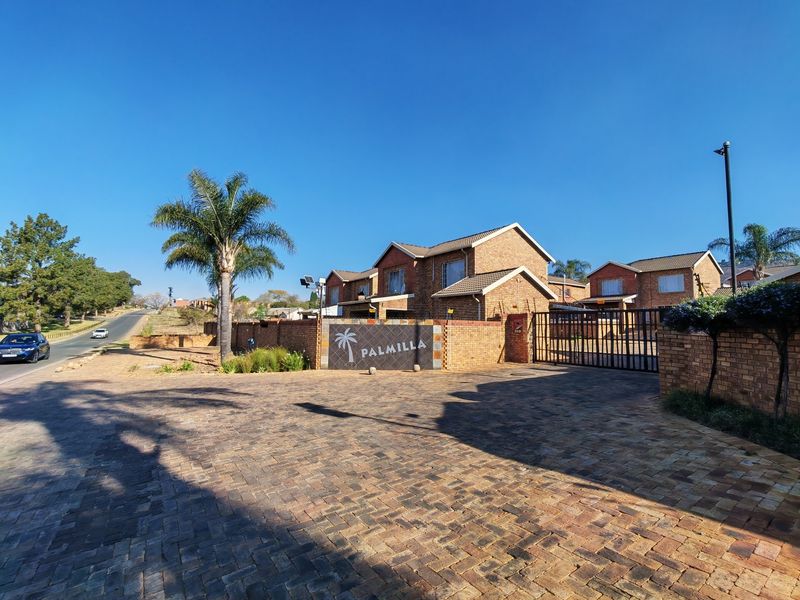 Front entrance view of the Palmilla townhouse complex featuring brick paving, a secure metal gate, and established brick boundary walls.