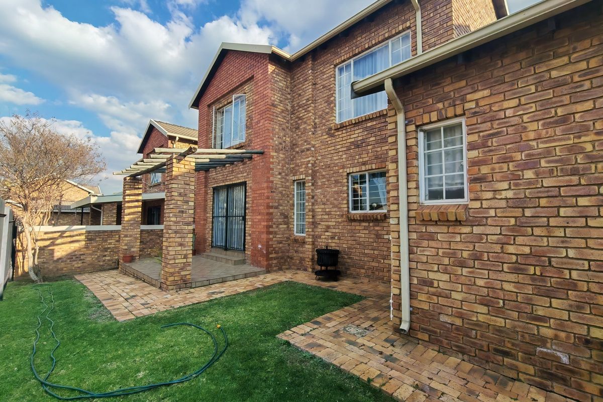Rear view of the townhouse featuring a face-brick facade, a covered brick pergola patio, paved walkways, and a private garden area.