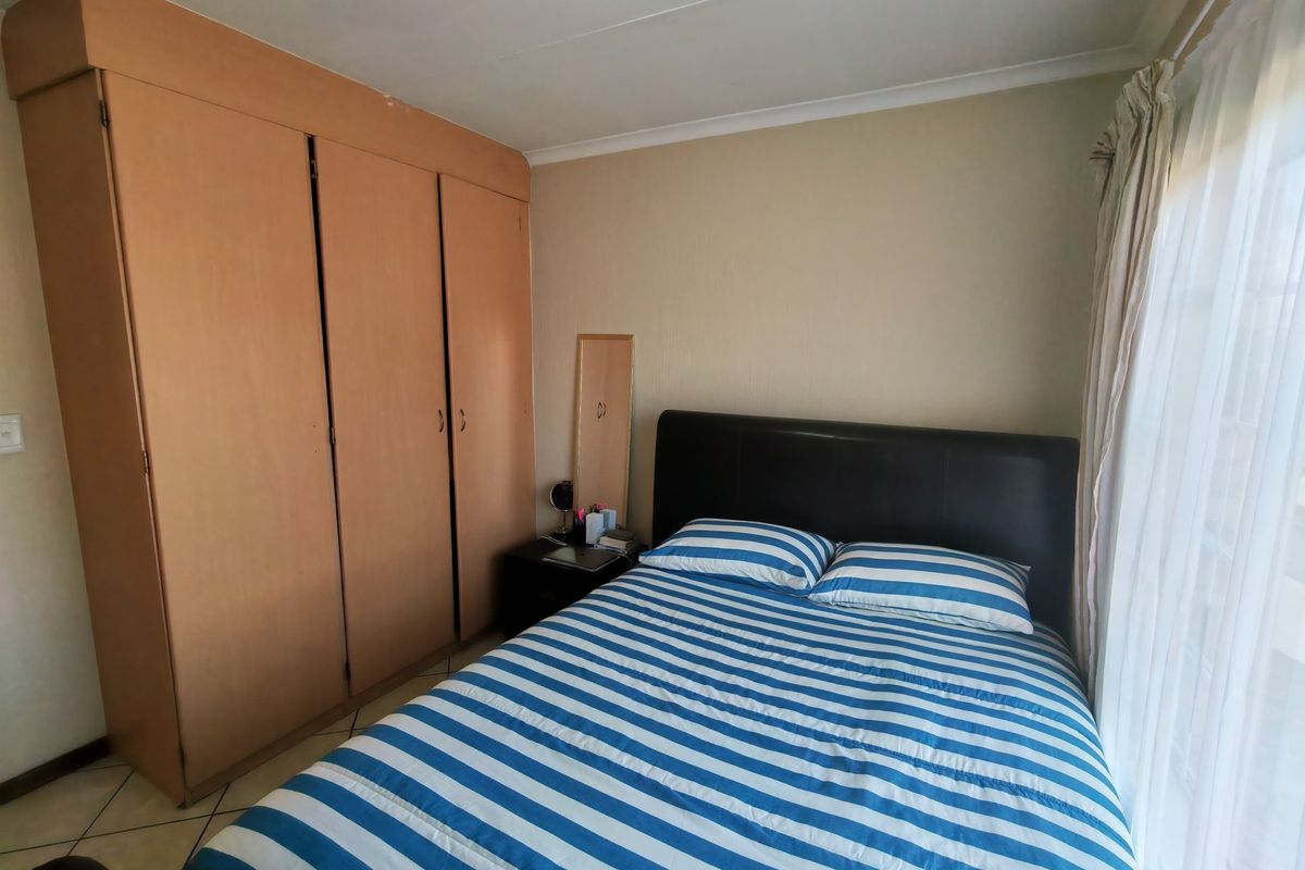A functional bedroom featuring built-in wooden cupboards, tiled flooring, and a coved ceiling, offering a practical layout with natural light.