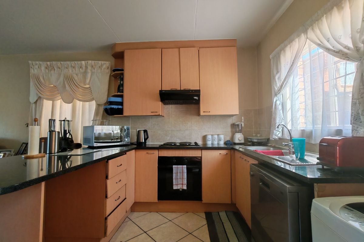A functional kitchen featuring light wood-tone cabinetry, dark granite countertops, built-in oven, hob, and extractor fan with tiled flooring and backsplash.
