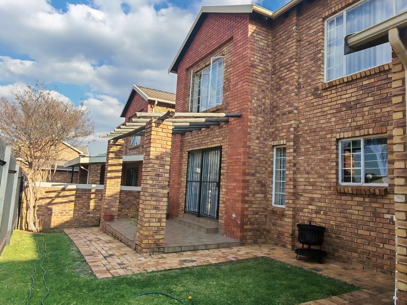 Rear view of a double-story face brick townhouse featuring a covered patio with a pergola, paved garden area, and secure access.