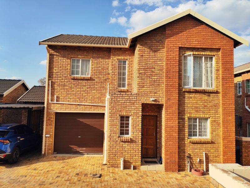 Front elevation of a double-storey face brick townhouse featuring a single garage, paved driveway, and traditional timber entrance door.