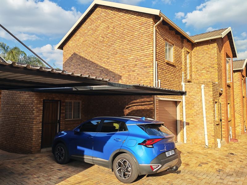 Exterior view of a face-brick townhouse featuring a paved driveway, a covered carport, and an integrated garage.