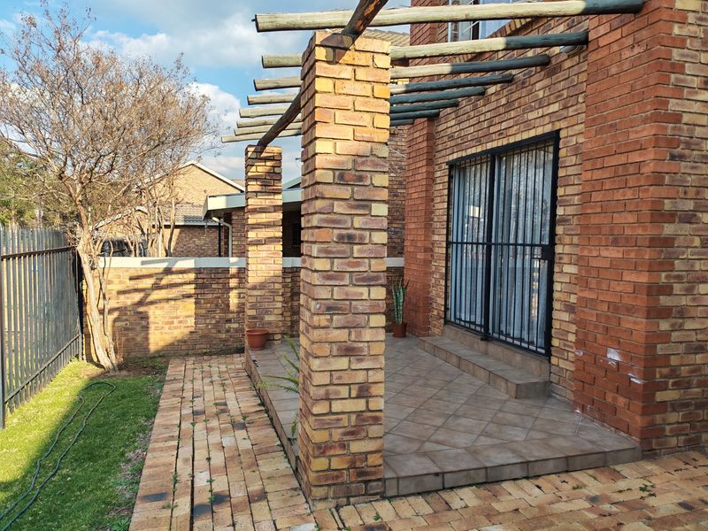 A private outdoor patio area featuring a brick pergola structure, tiled flooring, and direct access to the interior via a secure sliding door.