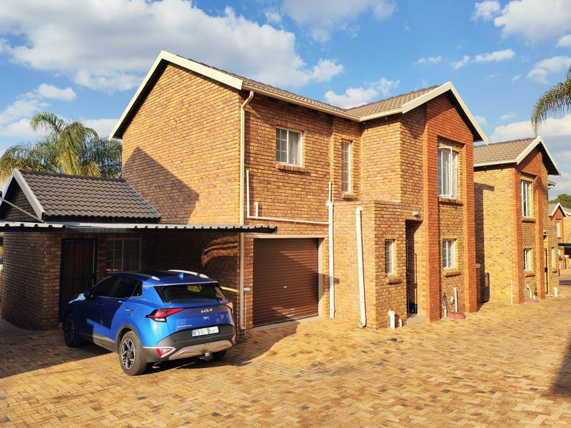 Front view of a double-storey face brick townhouse featuring a single garage, attached carport, and paved driveway.
