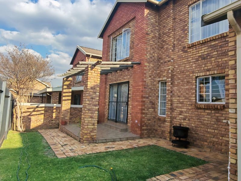 Rear view of a double-story townhouse featuring a face brick facade, a paved patio area with a pergola, and a small private garden.