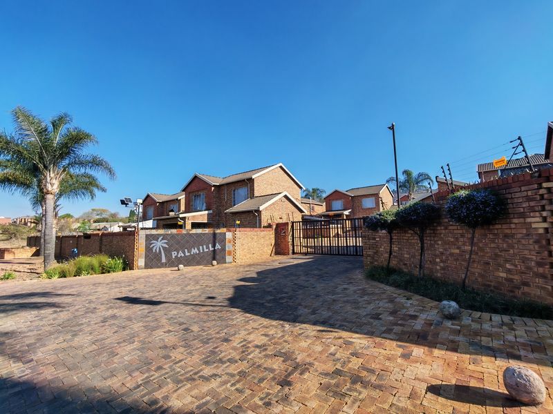 Front entrance view of the Palmilla townhouse complex featuring a paved driveway, brick boundary walls, and secure gated access.
