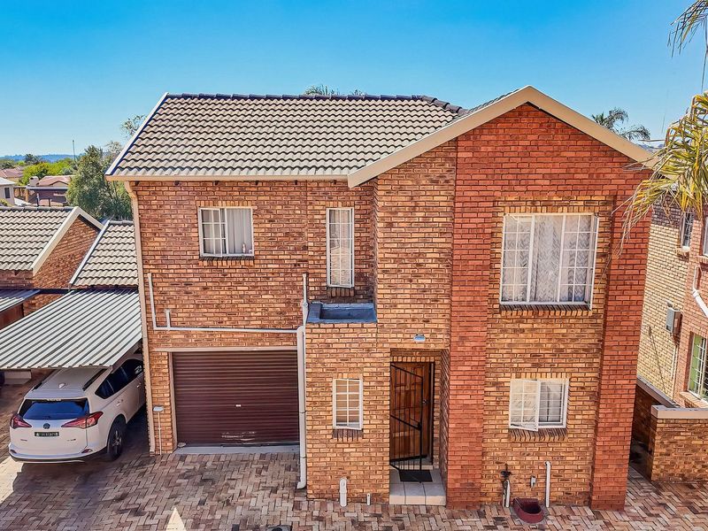 A two-story face brick townhouse featuring a tiled roof, a single garage, and an adjacent carport with paved driveway access.