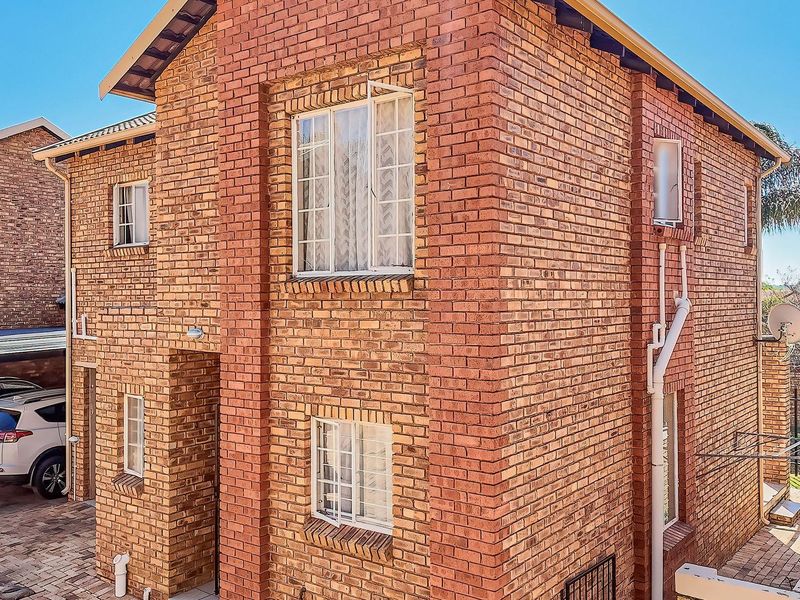 A well-maintained double-story face brick townhouse featuring a paved driveway and classic casement windows, presenting a solid and durable exterior facade.
