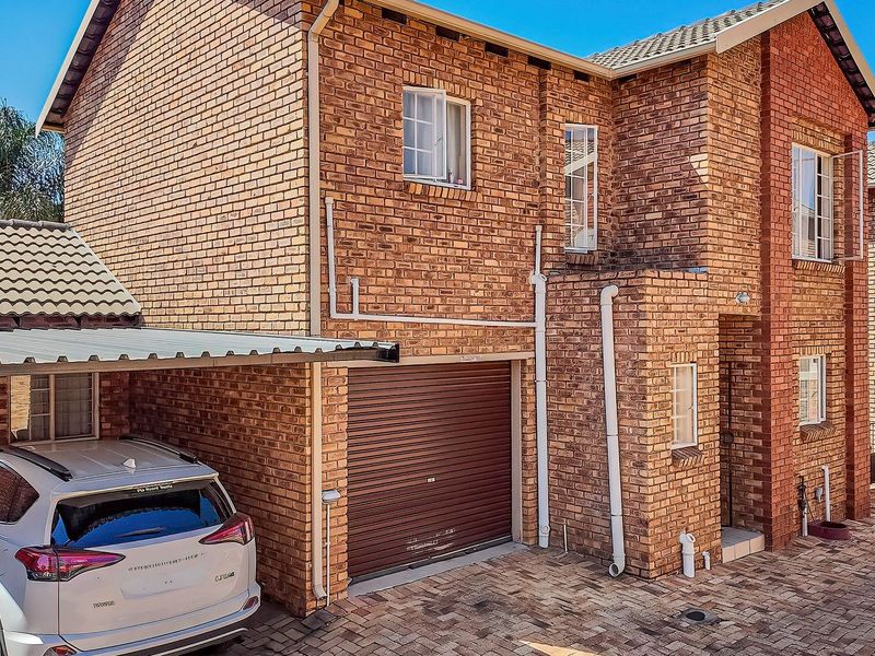 Front elevation of a double-story face brick townhouse featuring a paved driveway, integrated garage, and a covered carport.