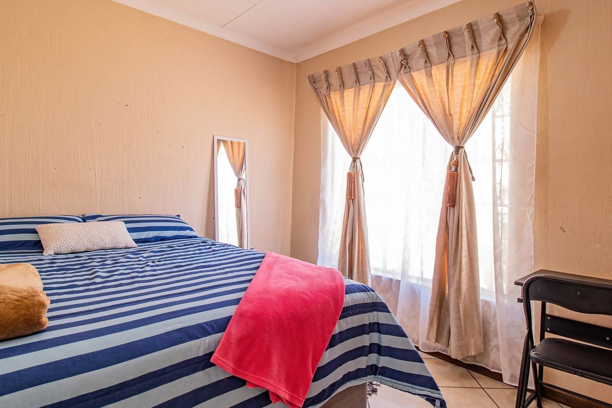 A standard bedroom featuring tiled flooring and textured walls, providing a functional space with natural light from the window.