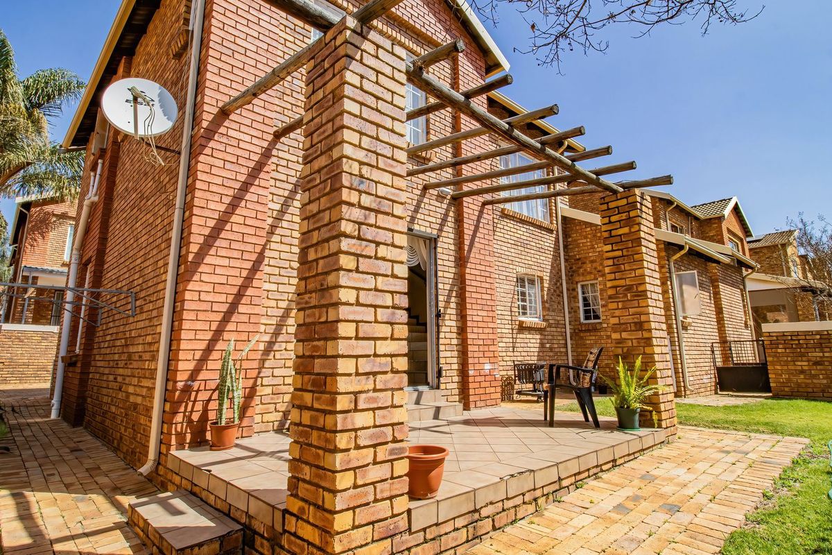 Rear exterior view of a townhouse featuring a brick facade, a tiled patio area with a timber pergola, and a surrounding paved garden path.