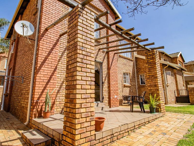 Rear exterior view of a townhouse featuring a brick facade, a tiled patio area with a timber pergola, and a surrounding paved garden path.