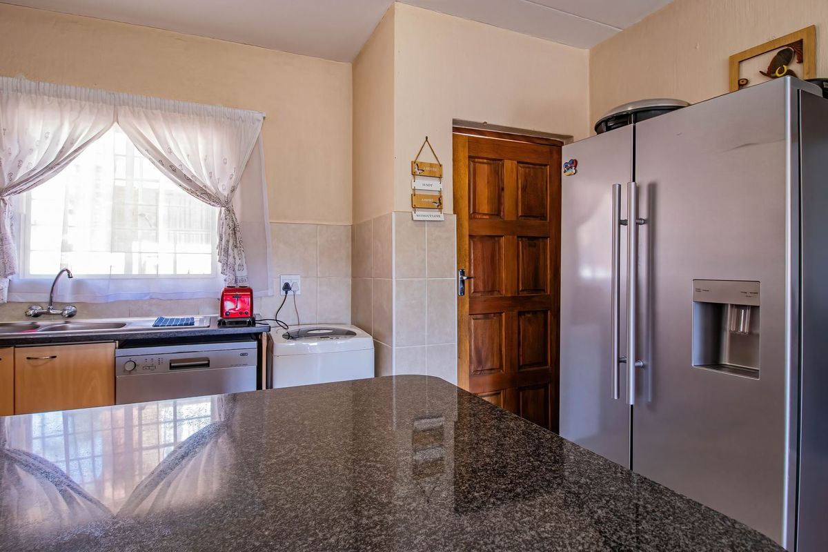 A functional kitchen featuring granite countertops, tiled backsplash, and wooden cabinetry, providing a practical workspace with direct access to an adjacent room.