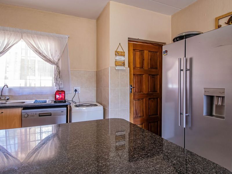 A functional kitchen featuring granite countertops, tiled backsplash, and wooden cabinetry, providing a practical workspace with direct access to an adjacent room.