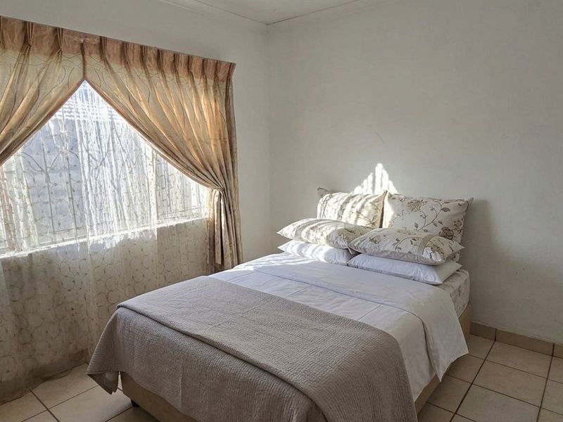 A simple bedroom featuring tiled flooring and a window fitted with security bars, providing natural light.