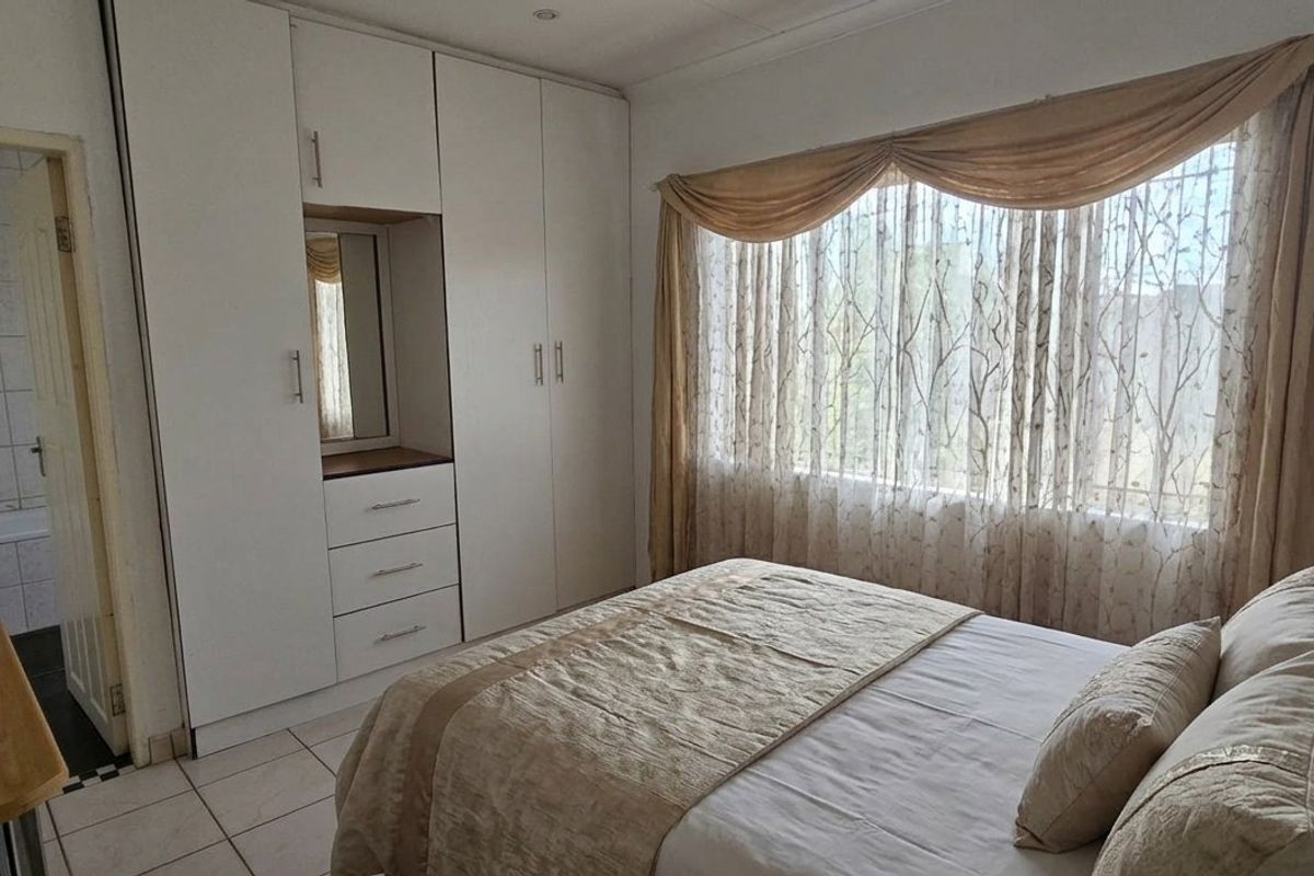 A bedroom featuring built-in cupboards, tiled flooring, and direct access to an en-suite bathroom with a bathtub.