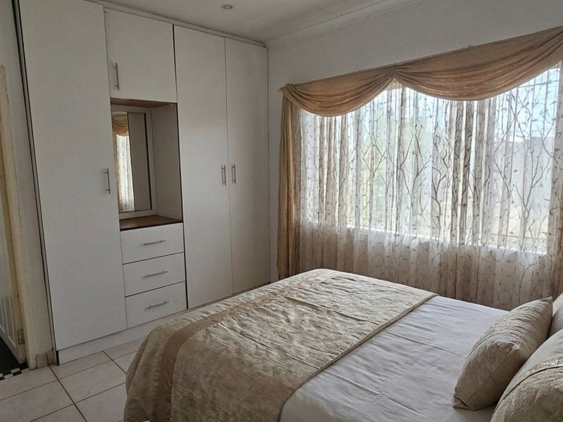 A bedroom featuring built-in cupboards, tiled flooring, and direct access to an en-suite bathroom with a bathtub.