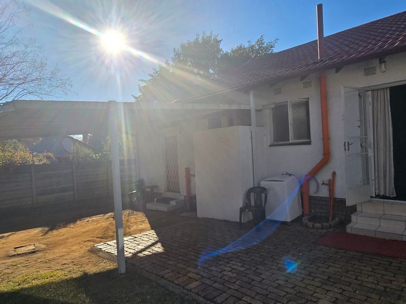 Rear exterior view of the house featuring a paved patio area, a covered carport, and direct access to the backyard.