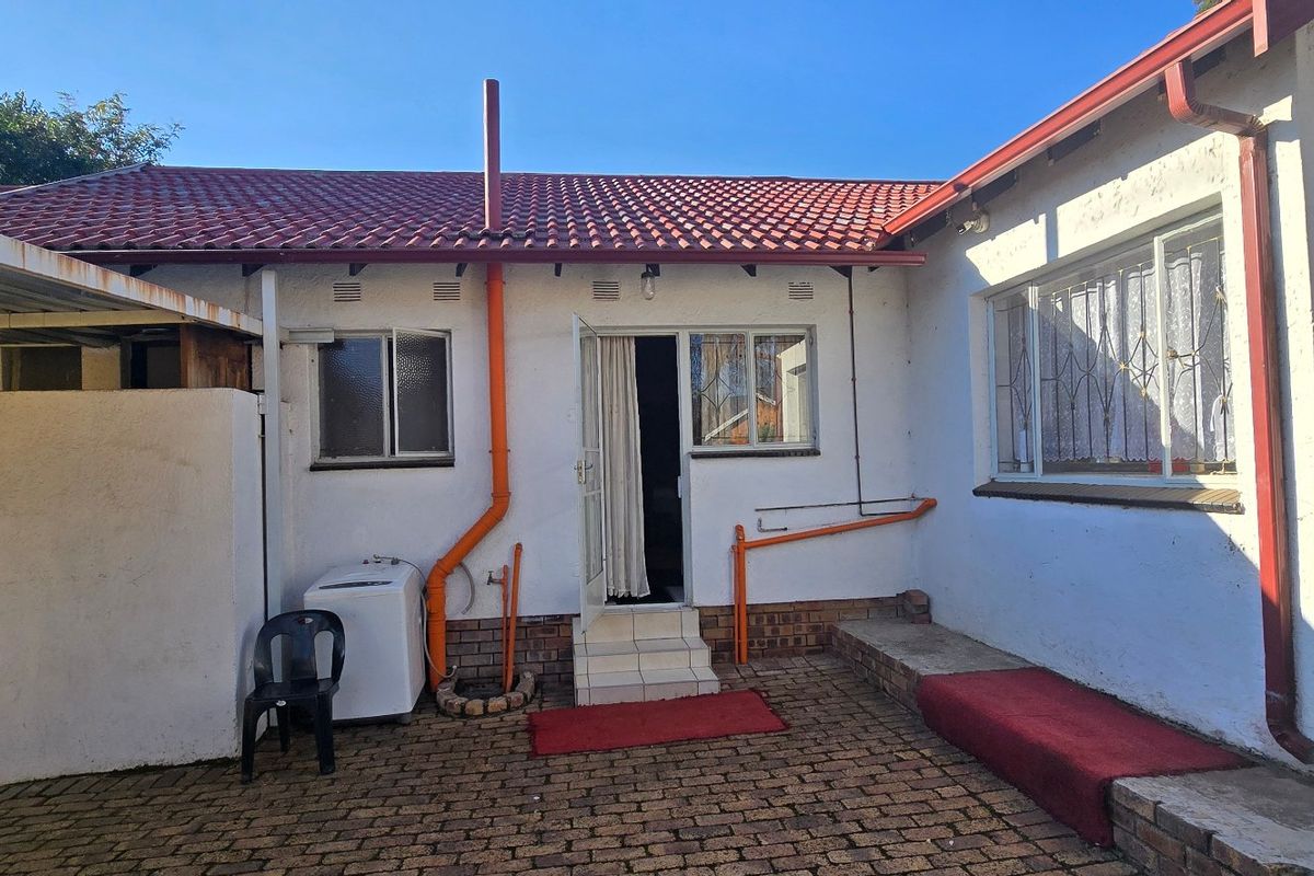 Rear exterior view of the property featuring a paved courtyard, tiled roof, and external access points with security gates.