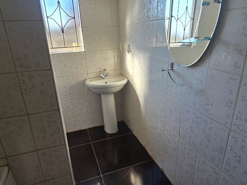 A functional bathroom featuring a pedestal basin, fully tiled walls, and dark floor tiles, providing a clean and practical space.