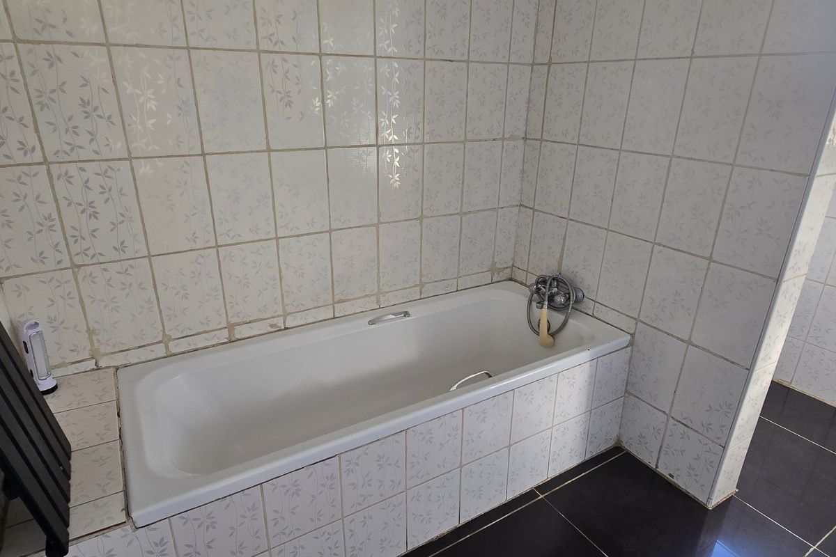 A functional bathroom featuring a built-in bathtub with tiled surround and flooring, offering a blank canvas for modern renovation.