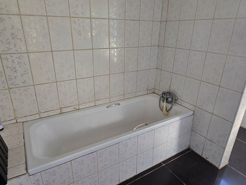 A functional bathroom featuring a built-in bathtub with tiled surround and flooring, offering a blank canvas for modern renovation.