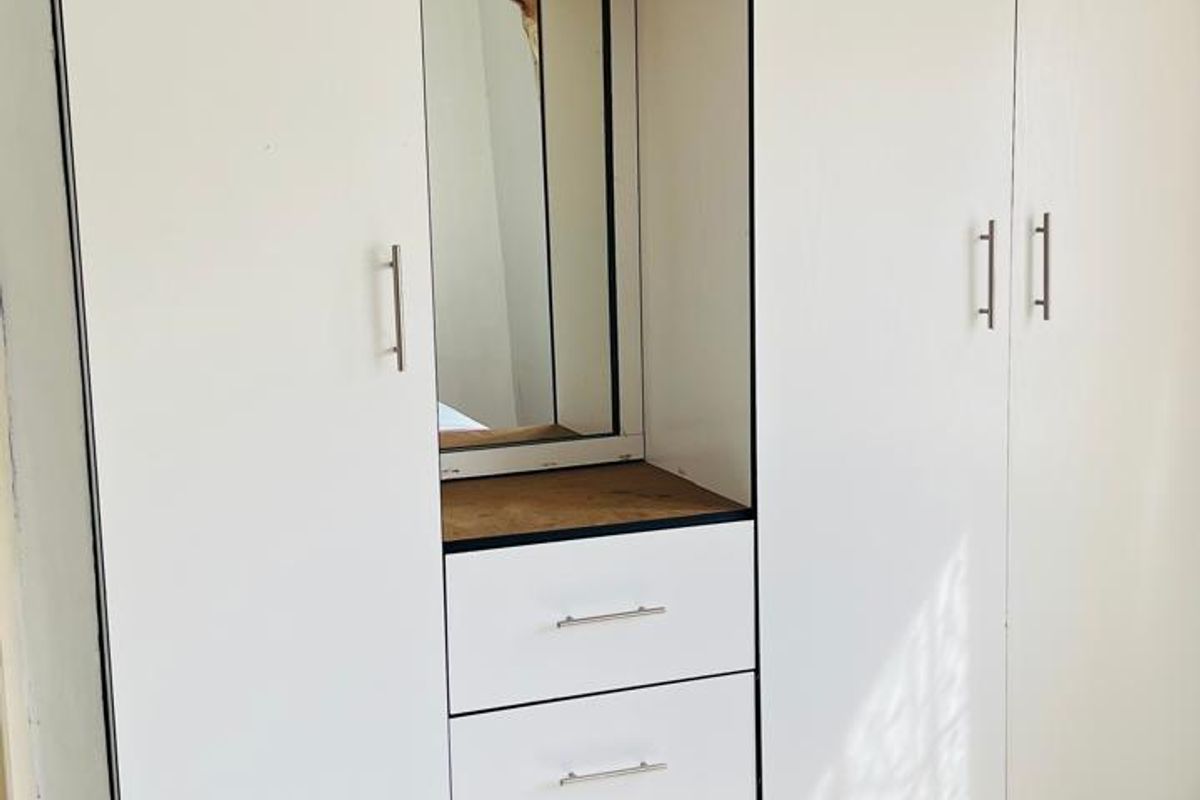 A bedroom featuring a white built-in wardrobe with integrated vanity, drawers, and tiled flooring.