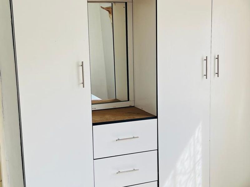 A bedroom featuring a white built-in wardrobe with integrated vanity, drawers, and tiled flooring.