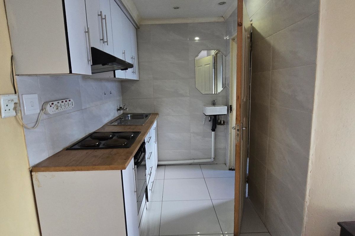 Compact kitchen featuring white cabinetry, wooden countertops, an electric hob, extractor fan, and tiled finishes with an adjacent wall-mounted basin.