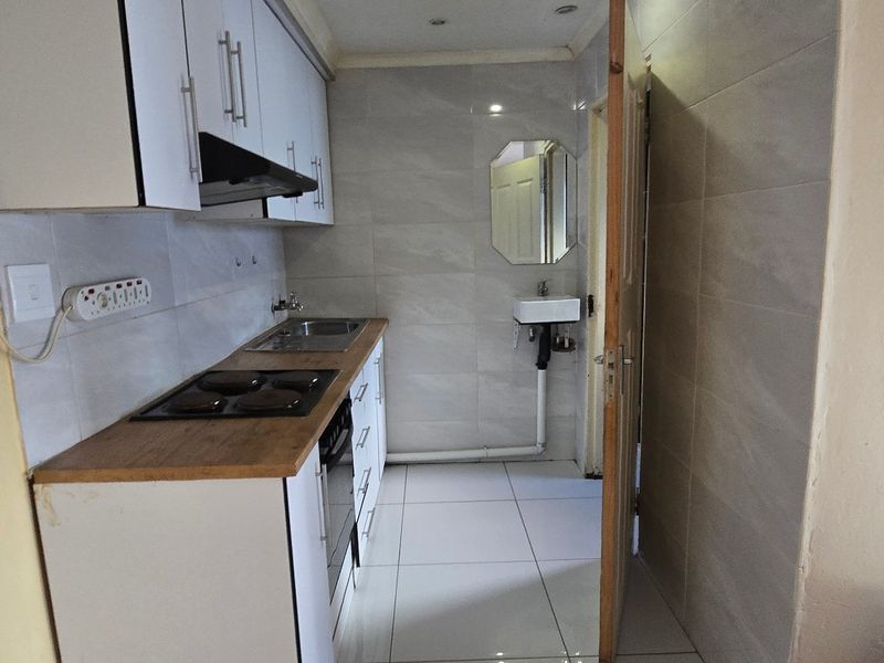 Compact kitchen featuring white cabinetry, wooden countertops, an electric hob, extractor fan, and tiled finishes with an adjacent wall-mounted basin.