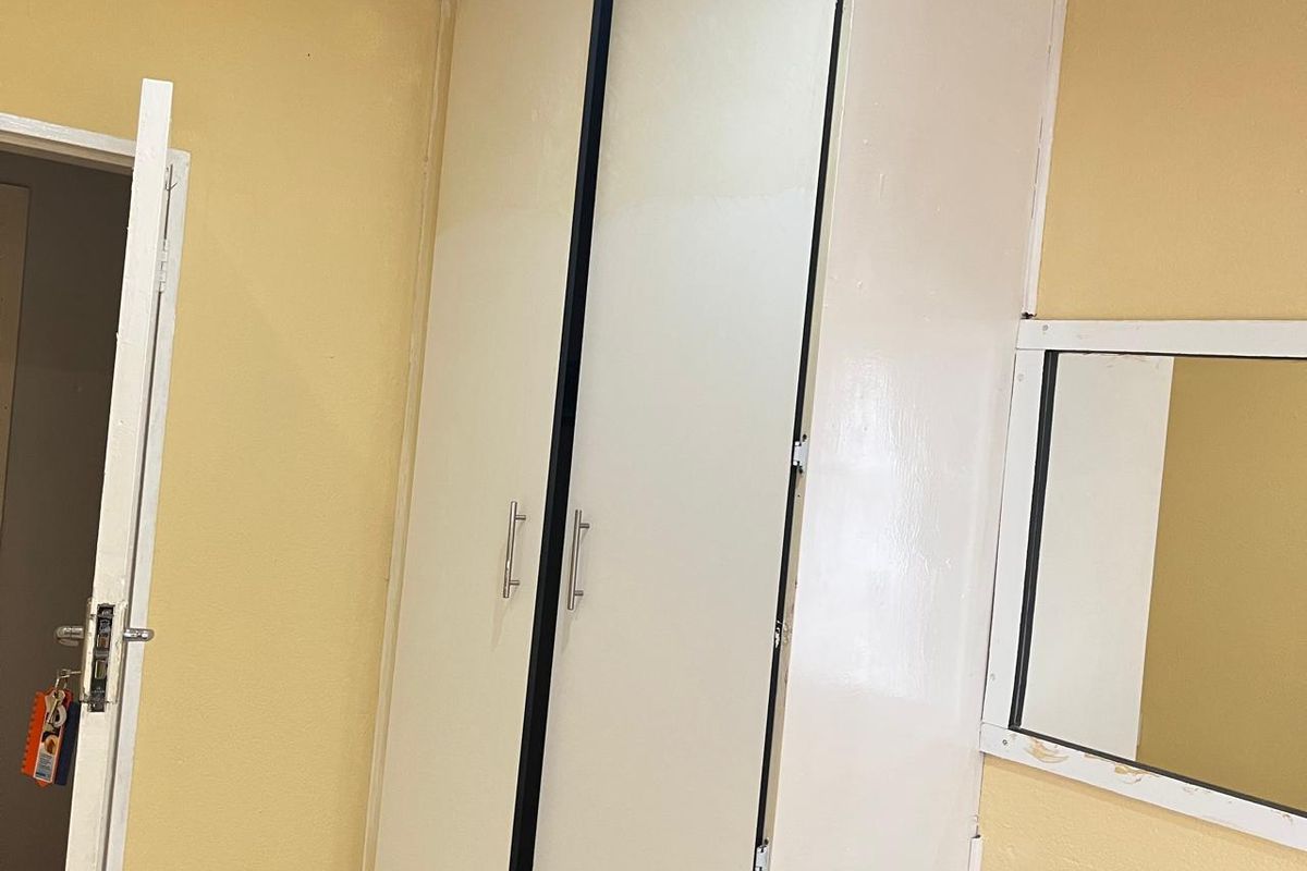 A bedroom featuring a built-in wardrobe and a wall-mounted mirror, requiring cosmetic updates to the paintwork and finishes.
