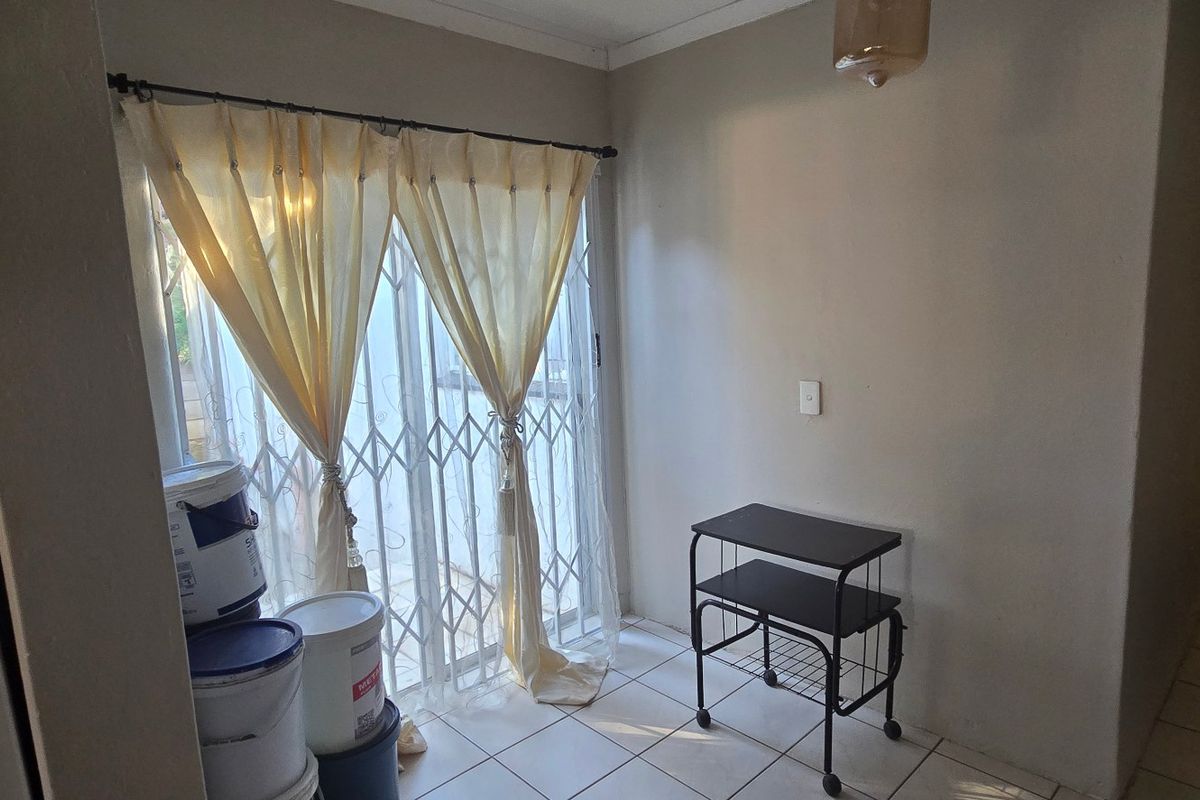 A simple, tiled living area featuring a sliding glass door with a security gate, providing access to the exterior.