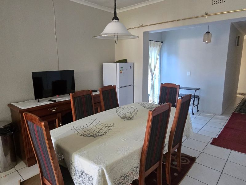A functional dining area featuring tiled flooring and a central pendant light, providing an open-plan layout that connects to the adjacent living and hallway spaces.