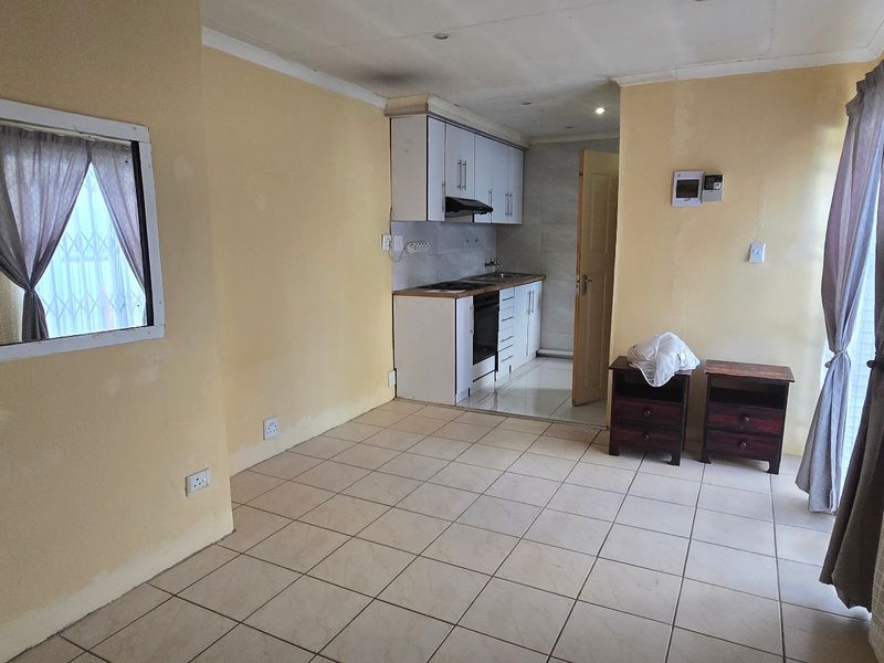 Open-plan living area featuring tiled flooring and a compact kitchen with built-in cabinetry, oven, and extractor fan.